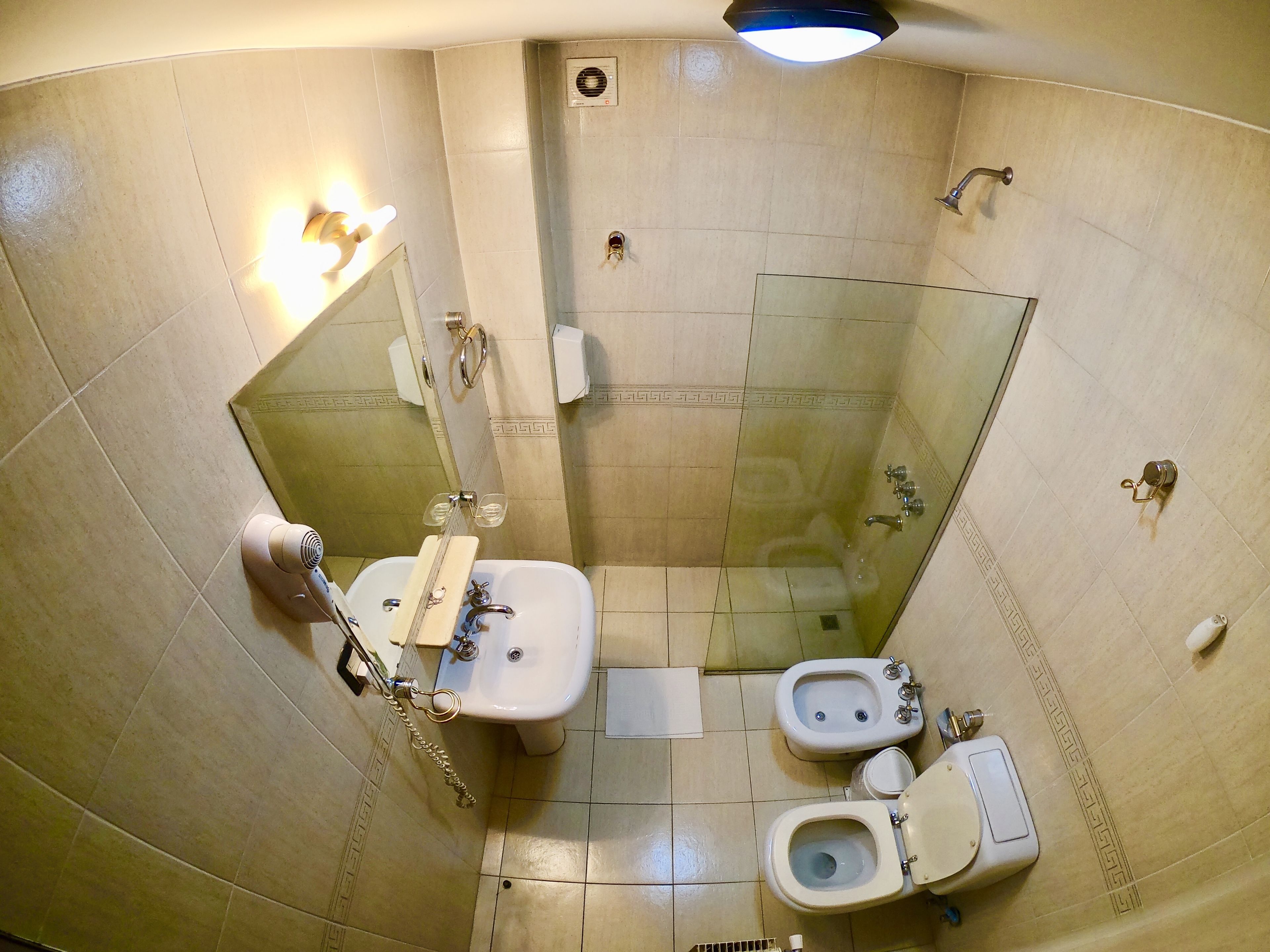 A compact bathroom with a shower, toilet, bidet, and sink.