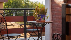Un pequeño patio exterior con una mesa de metal y dos sillas, una planta en maceta y un muro de ladrillo.