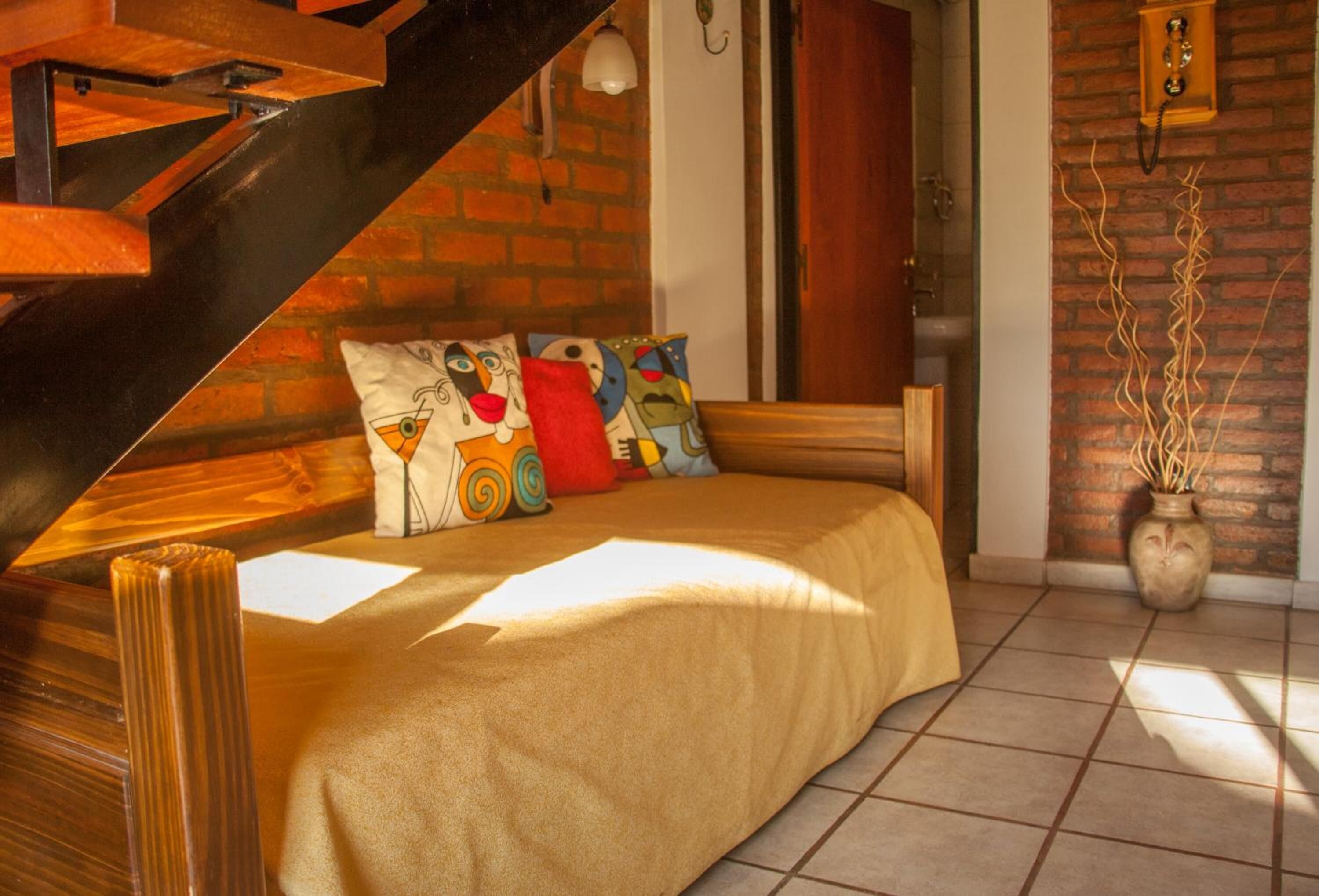 Un dormitorio acogedor con cama, almohadas coloridas, cabecero de madera, pared de ladrillo y lámpara colgante.