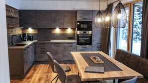 Een moderne keuken met donkere kasten, een houten eettafel en hanglampen.