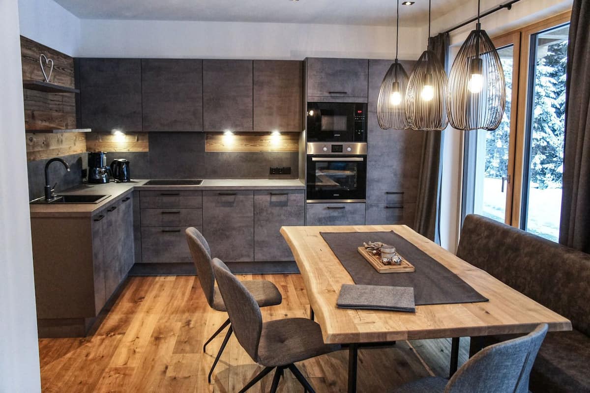 A modern kitchen with dark cabinets, a wooden dining table, and pendant lights.