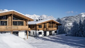 Een houten chalet met balkon, omringd door met sneeuw bedekte bergen en bomen.