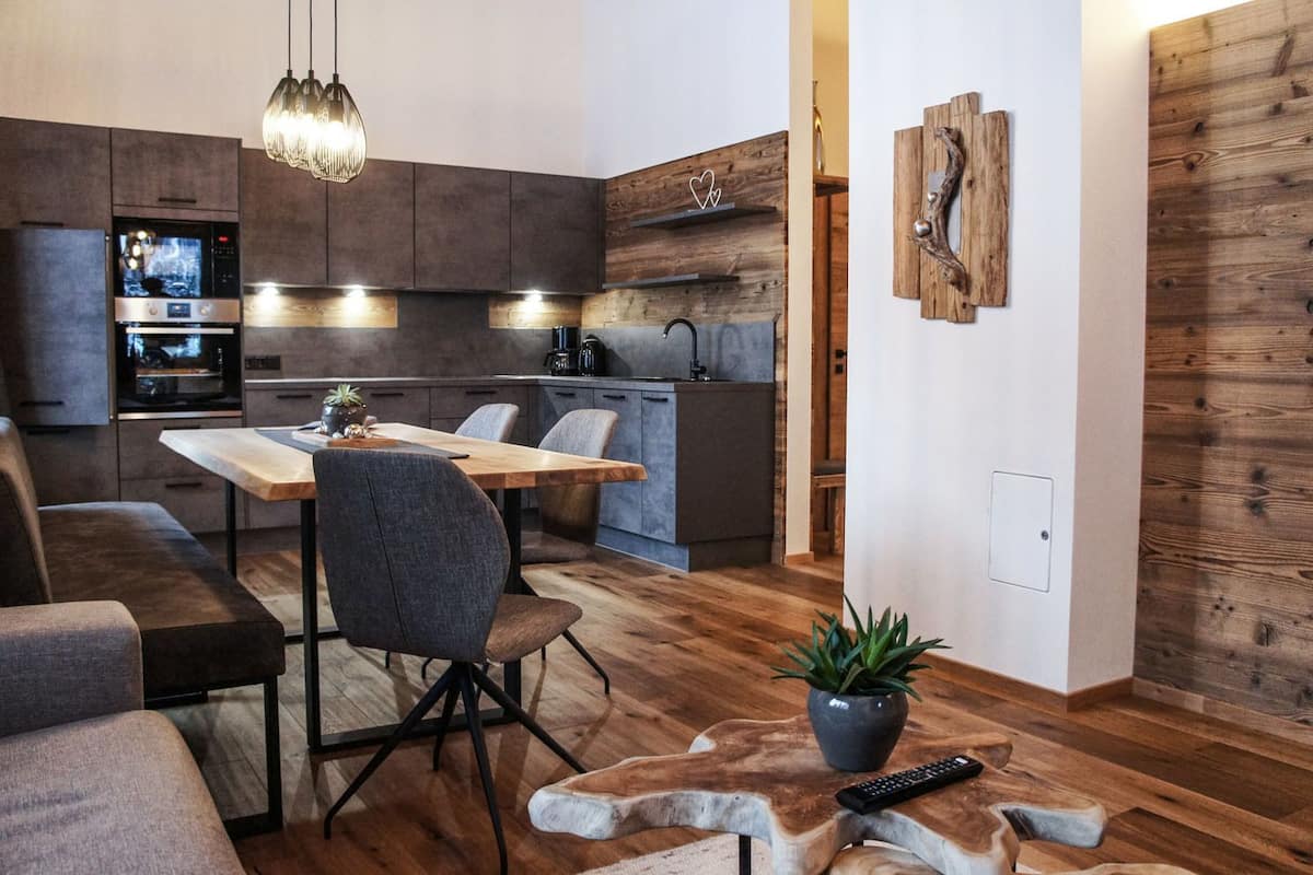 A modern kitchen with dark cabinets, a wooden dining table, and a built-in oven.