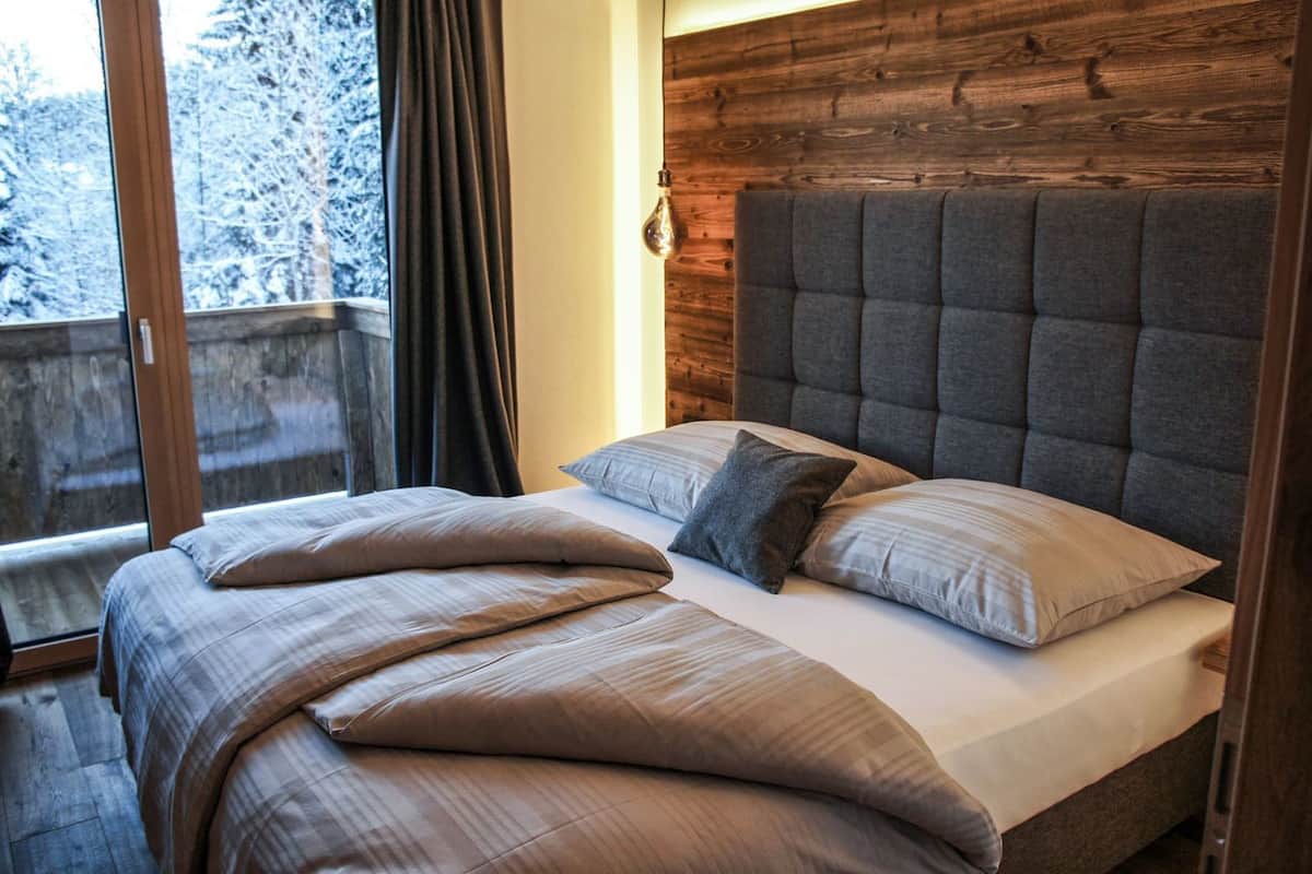 A bedroom with a large bed, wooden headboard, and a view of a snowy balcony.