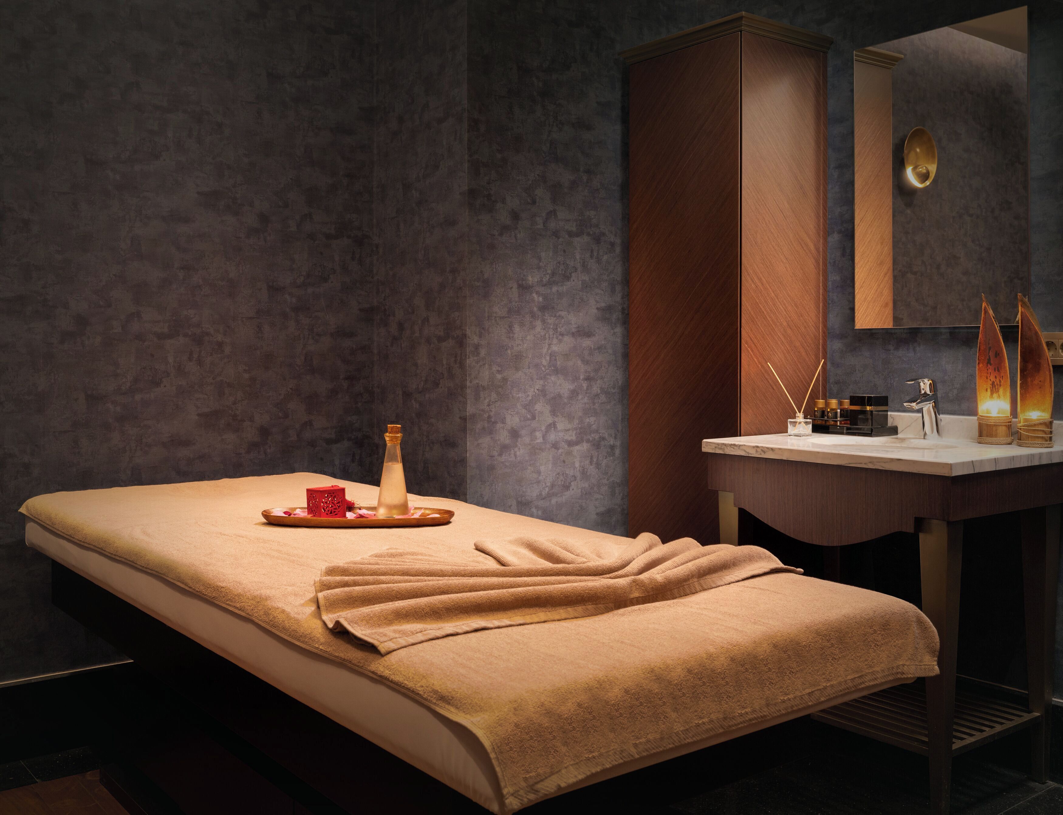 Ein Spa-Raum mit Massagetisch, Holzschrank, Schminktisch mit Spiegel und Kerzen.