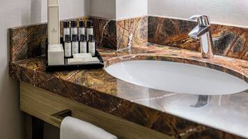 A bathroom with a marble countertop, a sink, a mirror, and a set of toiletries.