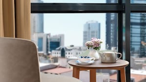 A modern room with a large window, a round wooden table with a vase of flowers, and a beige chair. - Gleam Bomonti Hotel (Istanbul)