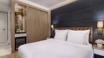 A modern hotel room with a large bed, a minibar, a wooden wardrobe, and a dark accent wall.