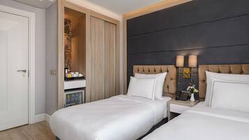 A hotel room with two beds, a minibar, a bedside table with a lamp, and a dark headboard.