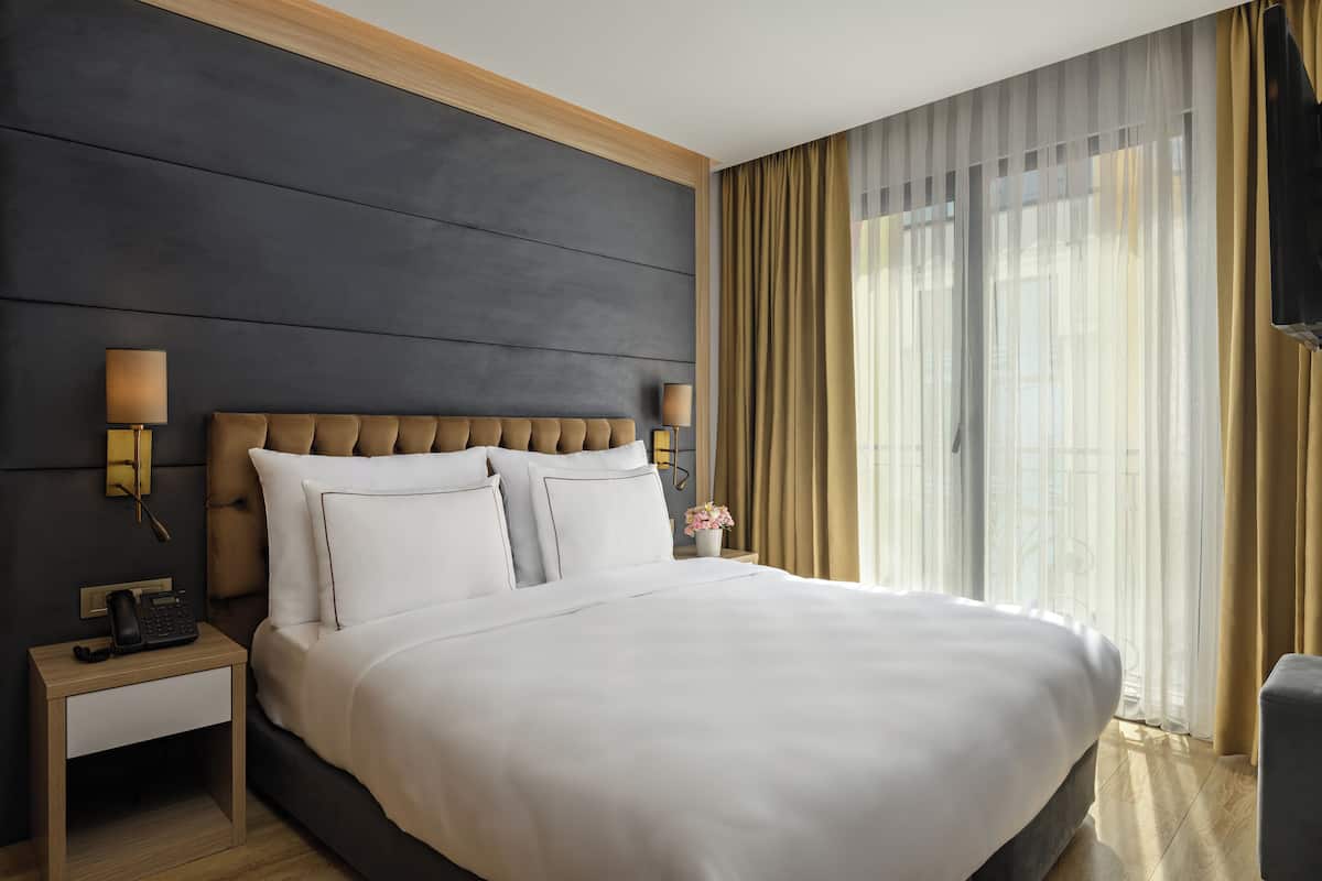 Una habitación de hotel moderna con una cama grande, una mesita de noche de madera y una lámpara de noche.