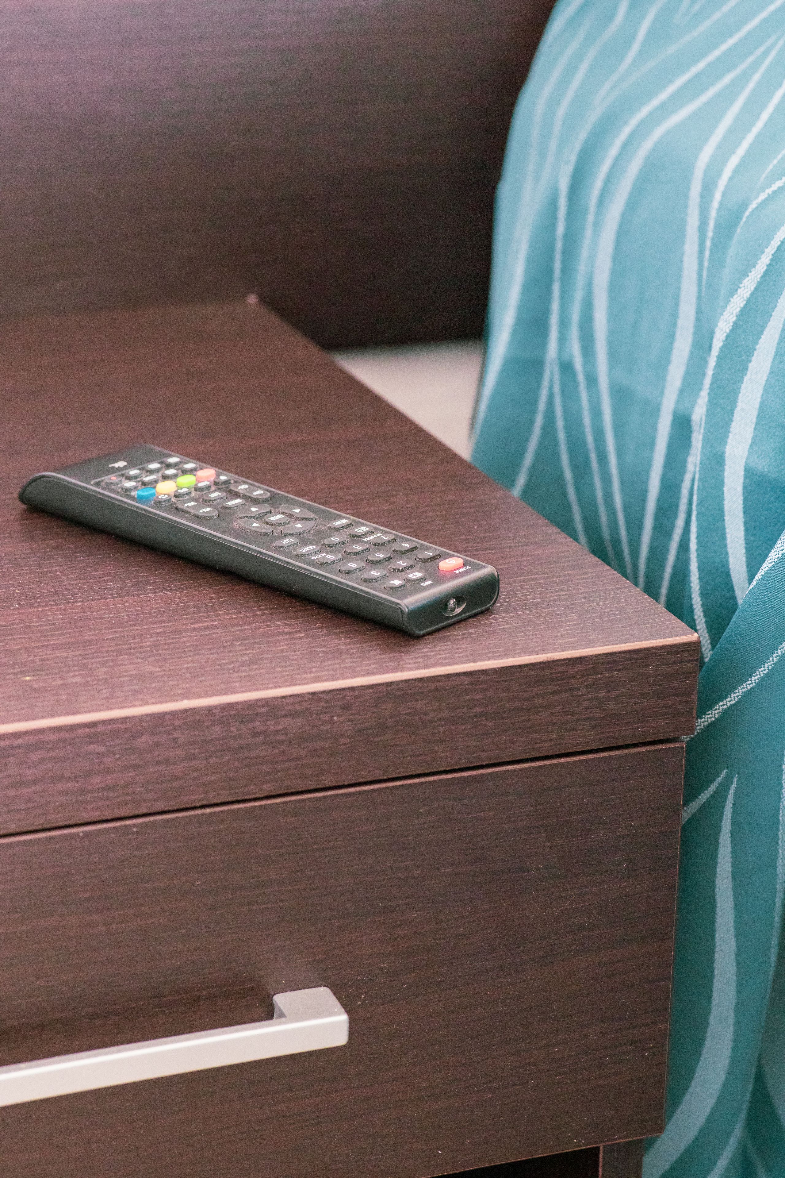 A remote control on a wooden nightstand with a drawer.