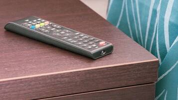 A remote control on a wooden nightstand with a drawer.