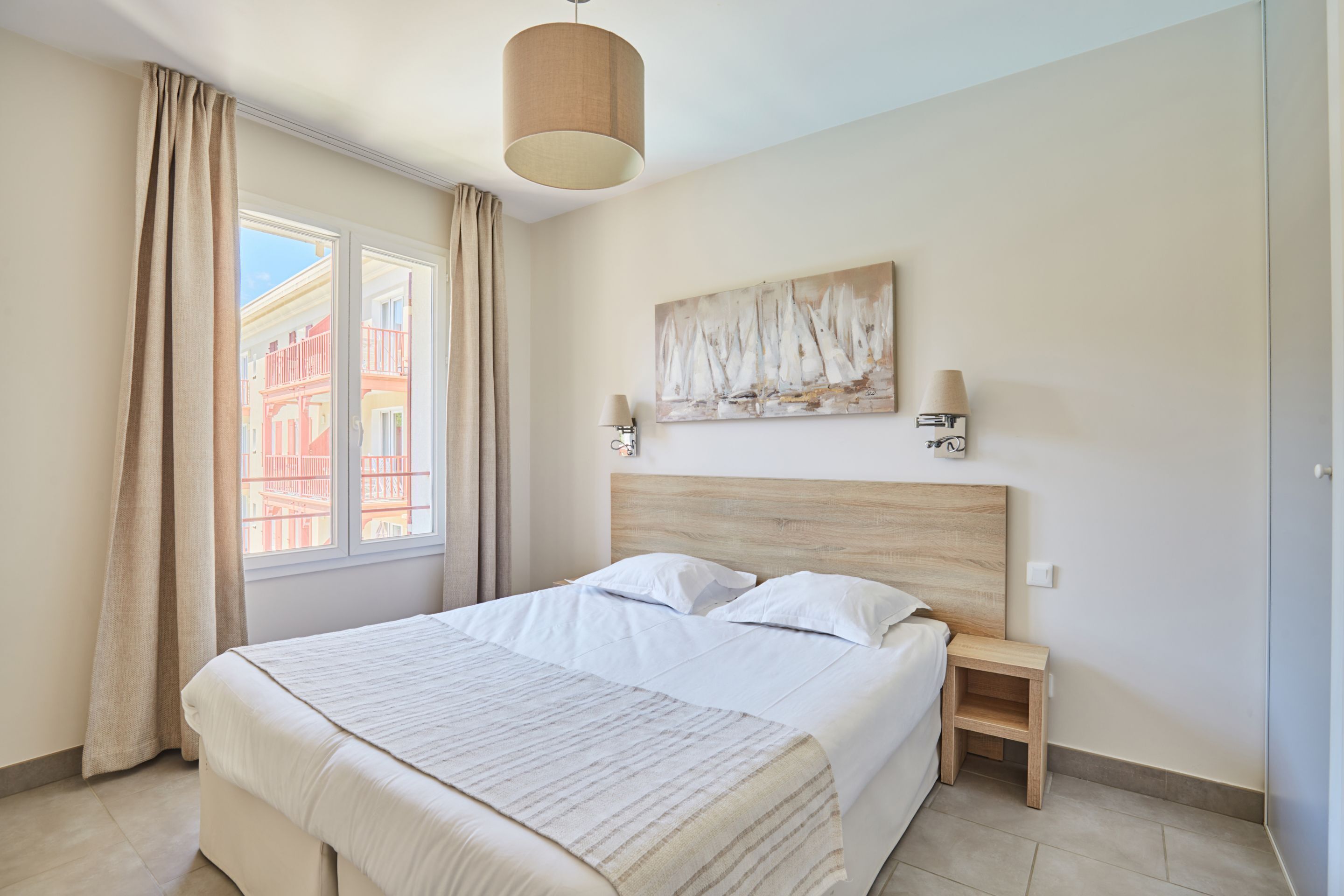 Un dormitorio moderno con una cama grande, una mesita de noche, una lámpara de pared y una ventana con cortinas.
