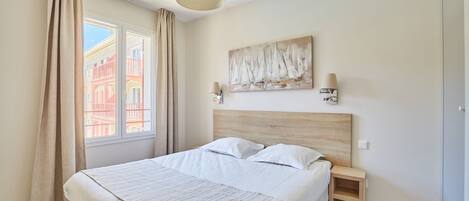 Un dormitorio moderno con una cama grande, una mesita de noche, una lámpara de pared y una ventana con cortinas.