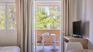 Una habitación con balcón, una cama, un escritorio, un televisor y vistas a árboles.
