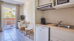 Una cocina compacta con microondas, lavamanos y un refrigerador pequeño. Se ve un comedor con una mesa y sillas a través de una puerta abierta.