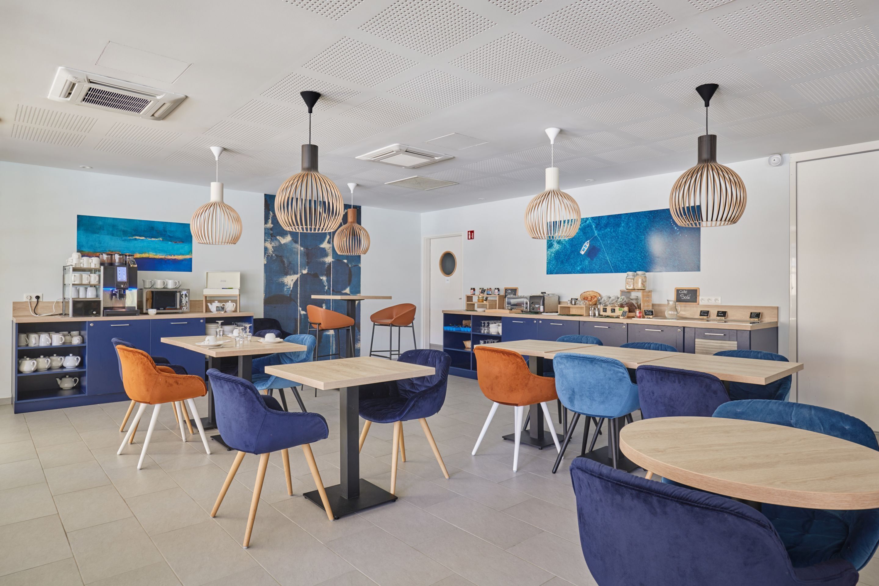 A modern cafe with multiple seating areas, including tables and chairs, and a counter with a coffee machine.
