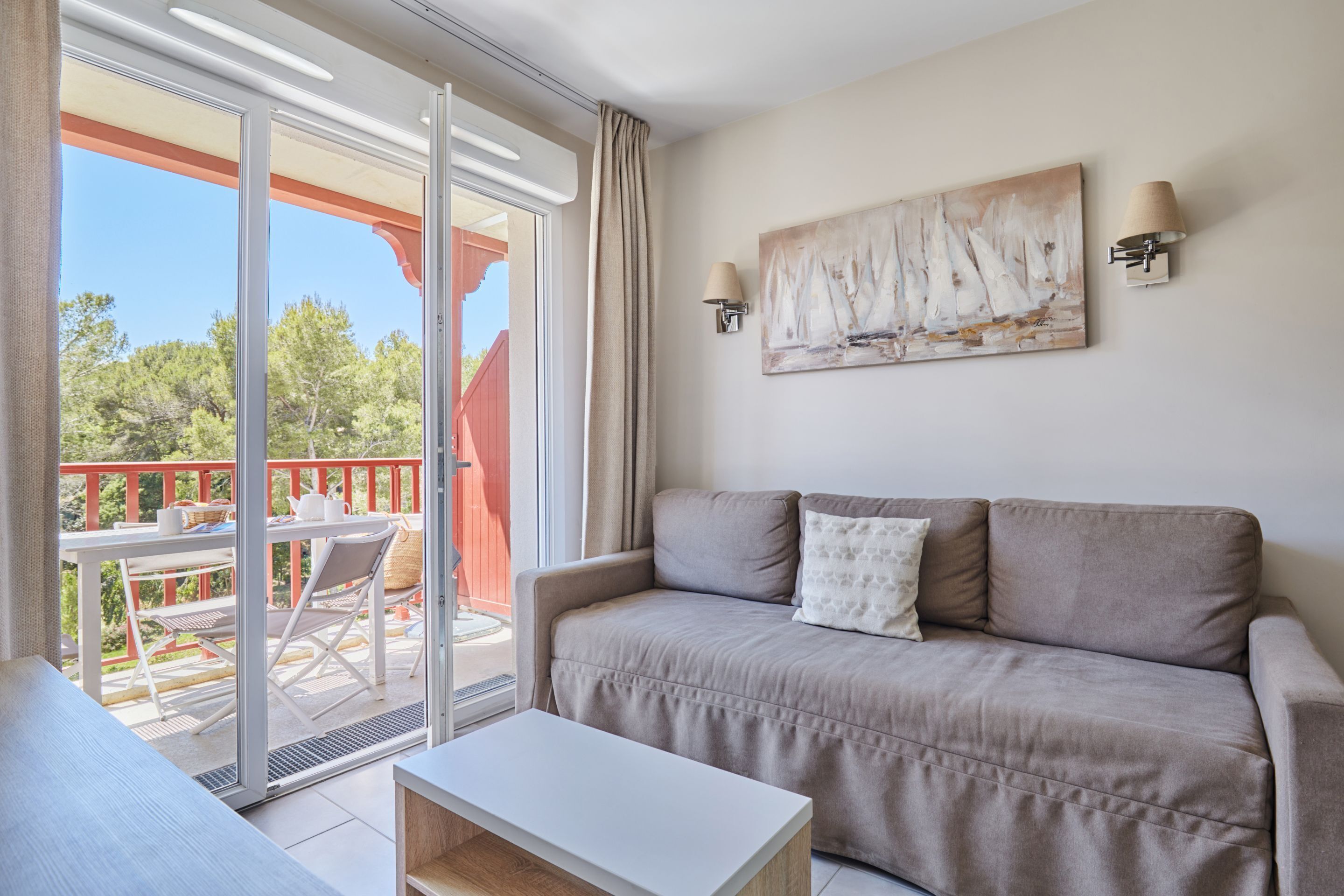 Una sala de estar con un sofá color beige, una mesa de centro blanca y un cuadro con barcos de vela en la pared.