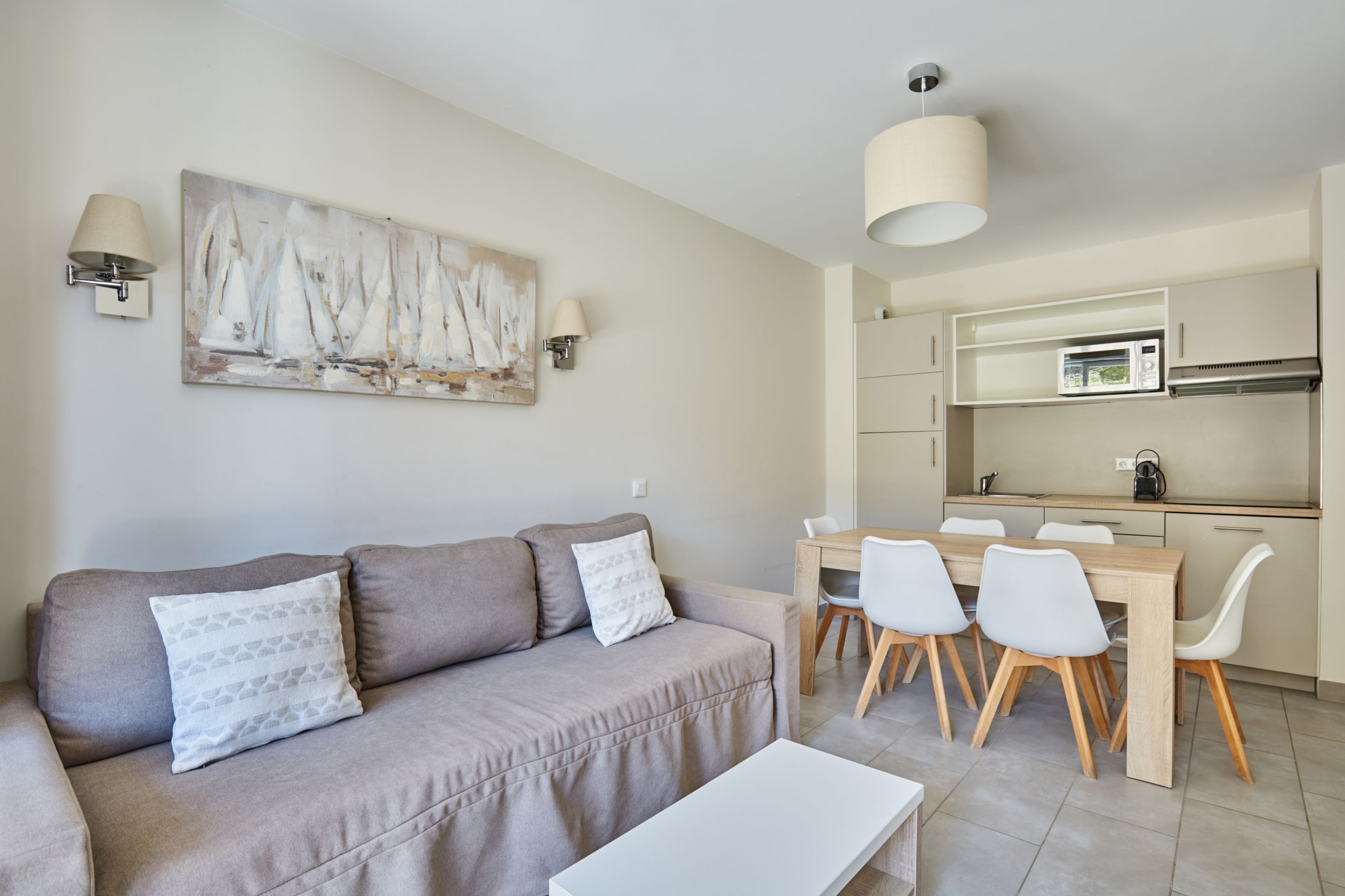 Una sala moderna con un sofá, una mesa de comedor con sillas, una zona de cocina con microondas y un cuadro en la pared.