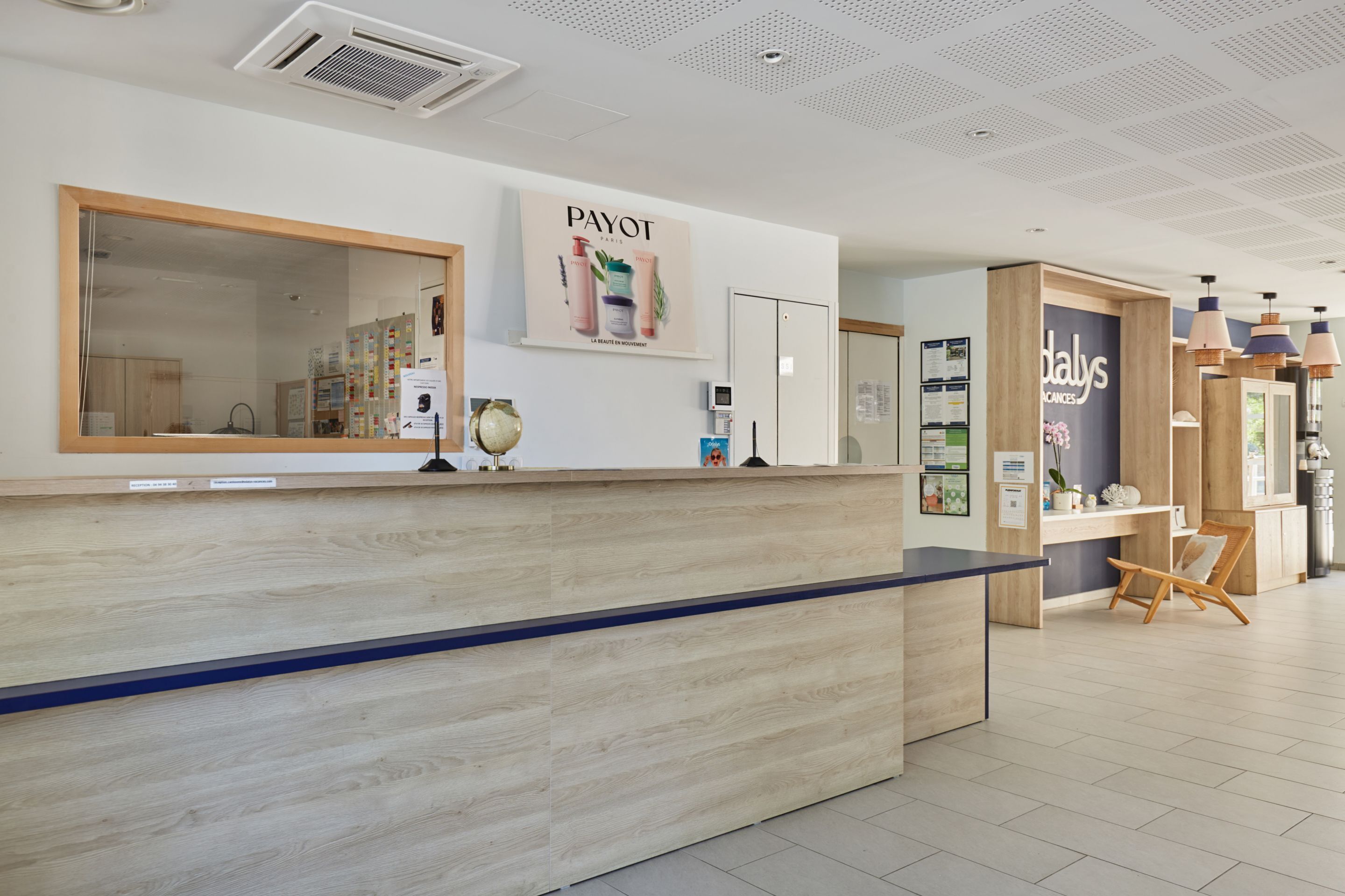 Un'area di accoglienza con una reception in legno, un grande specchio e il cartello 'PAYOT'.