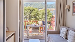 Un balcón con mesa y sillas, un sofá y vistas a árboles y edificios.