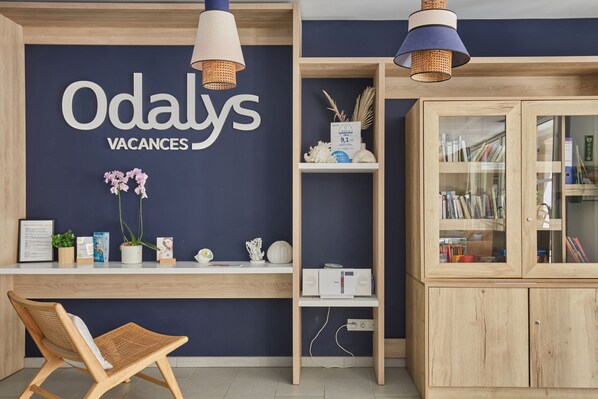 Un espace d’accueil avec un mur bleu foncé, un bureau en bois, des chaises en osier et un meuble avec des portes en verre.
