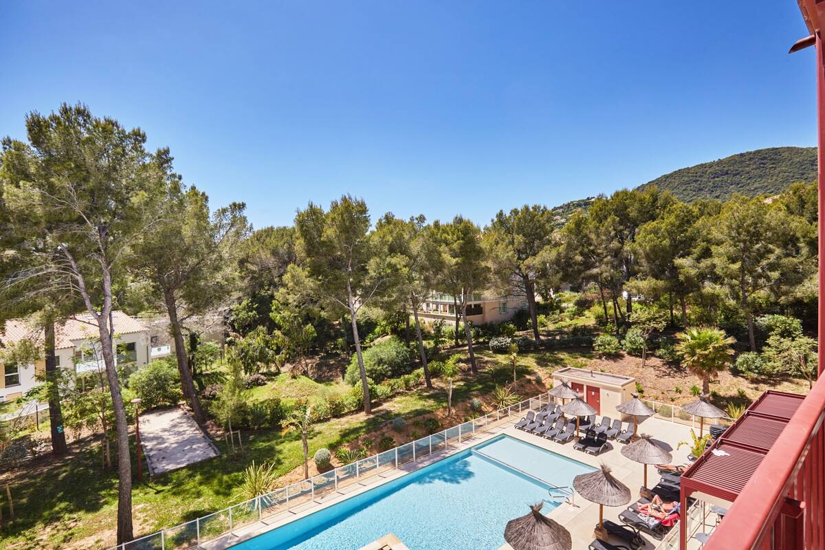 Ein Poolbereich mit Liegestühlen und Sonnenschirmen, umgeben von Bäumen und einem Berg im Hintergrund.