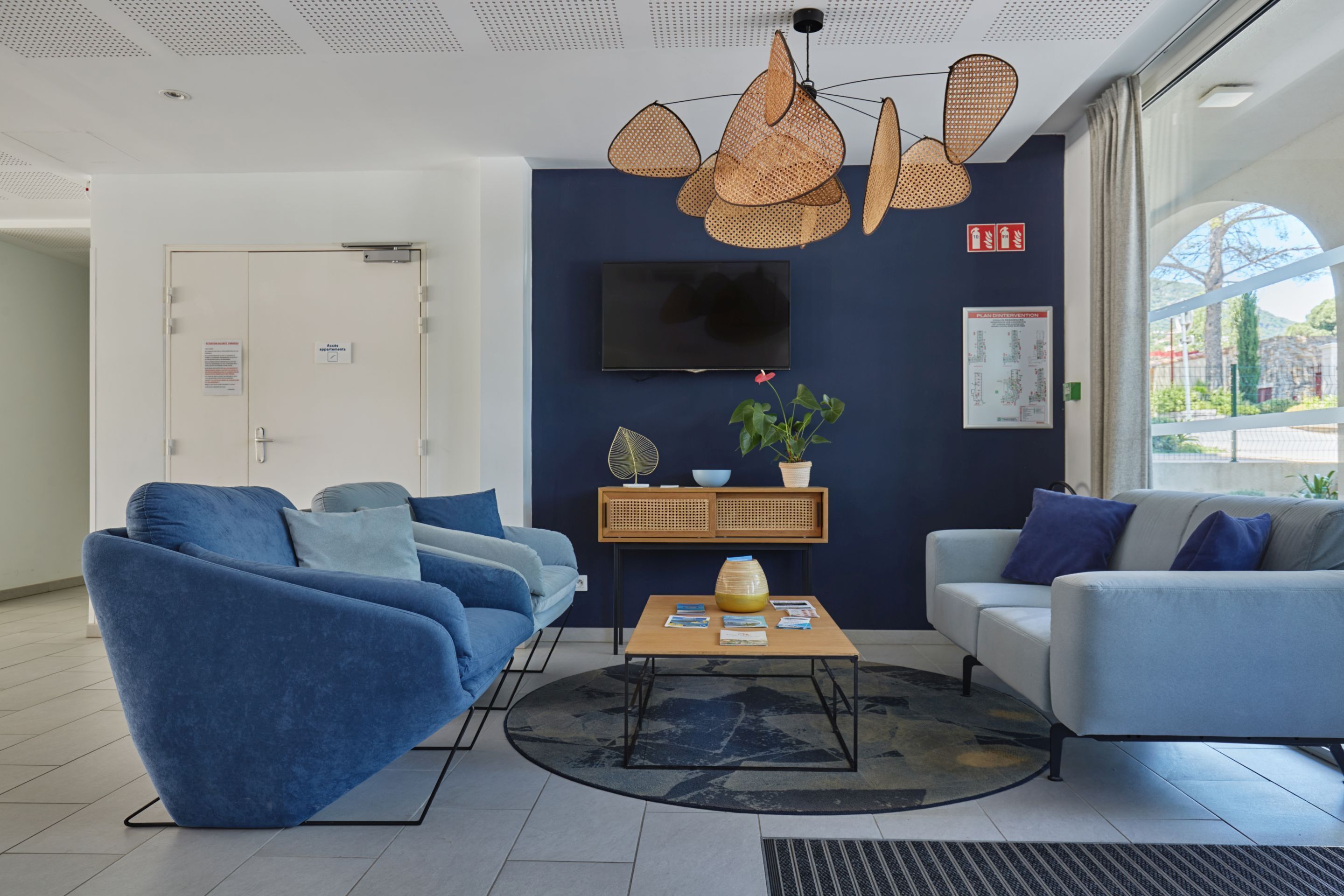 Un espace d’accueil moderne comprenant deux canapés, une table basse, un téléviseur et une grande fenêtre.