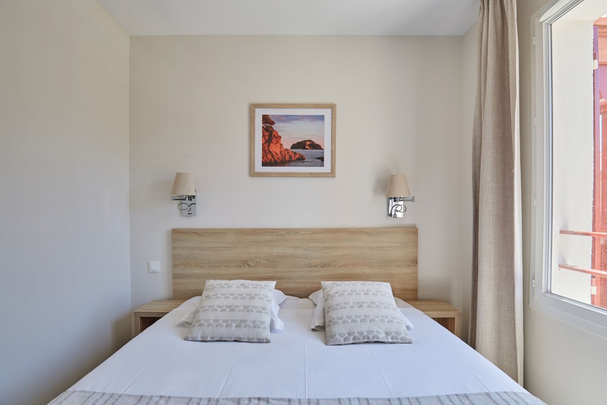 A neatly made bed with two pillows, a wooden headboard, bedside lamps, and a framed picture on the wall.