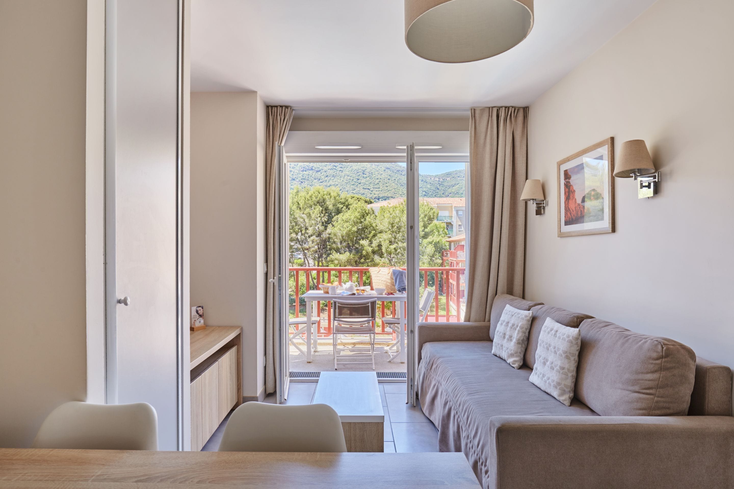 Una camera d'albergo moderna con un balcone, un divano, un tavolo da pranzo e vista sull'esterno.