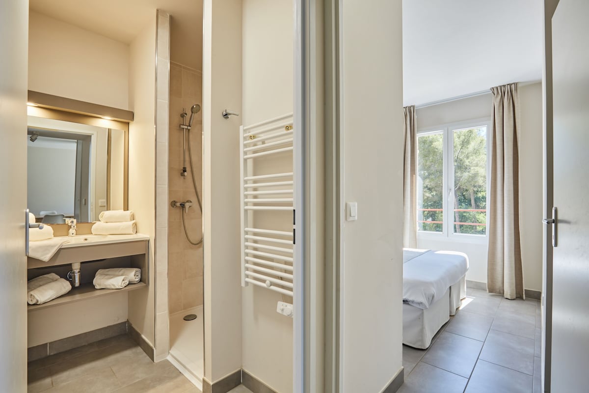 A hotel bathroom with a shower, a sink with a mirror, and a towel rack.