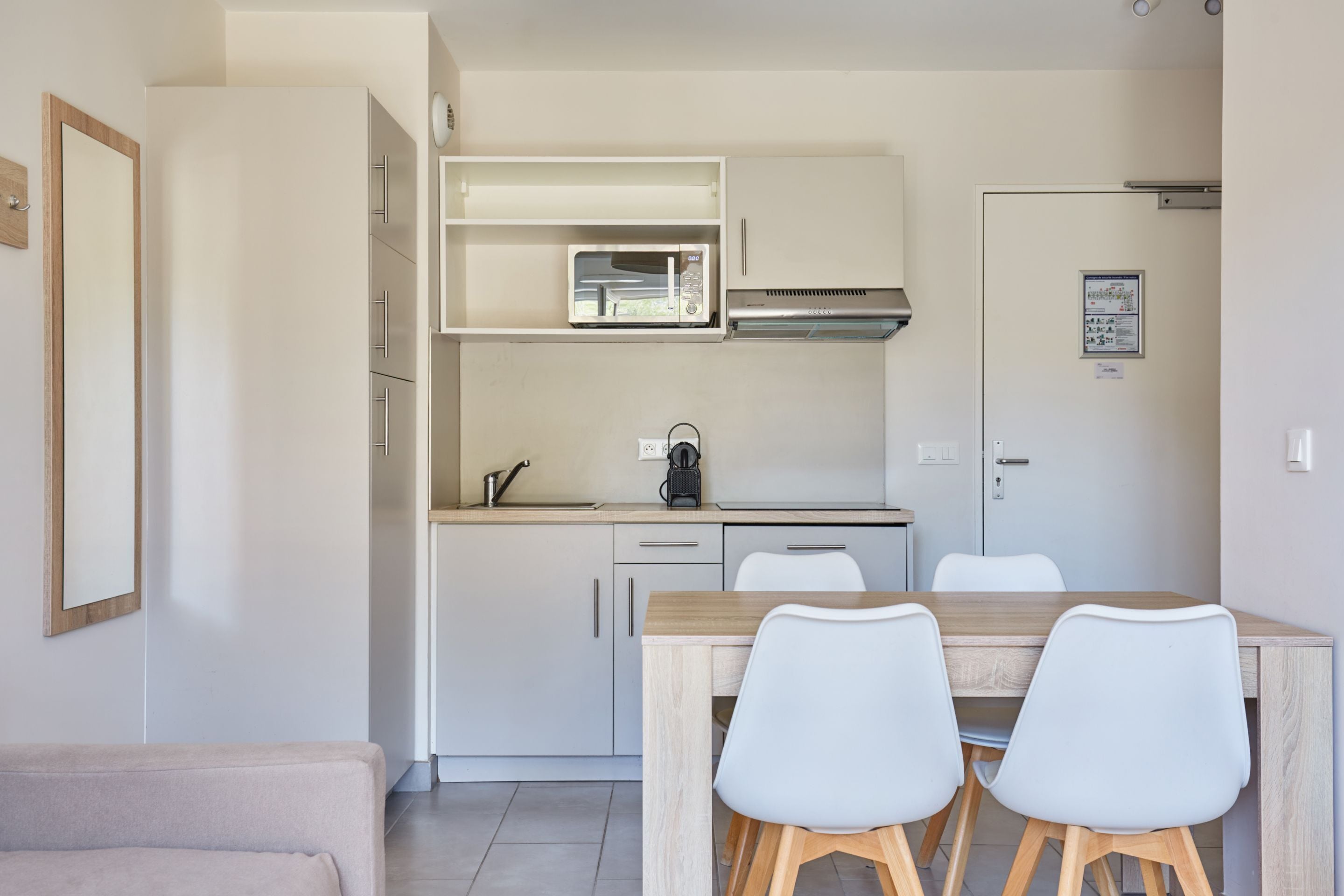 A compact kitchen with white cabinets, a microwave, and a coffee maker. There is a dining table with four chairs.