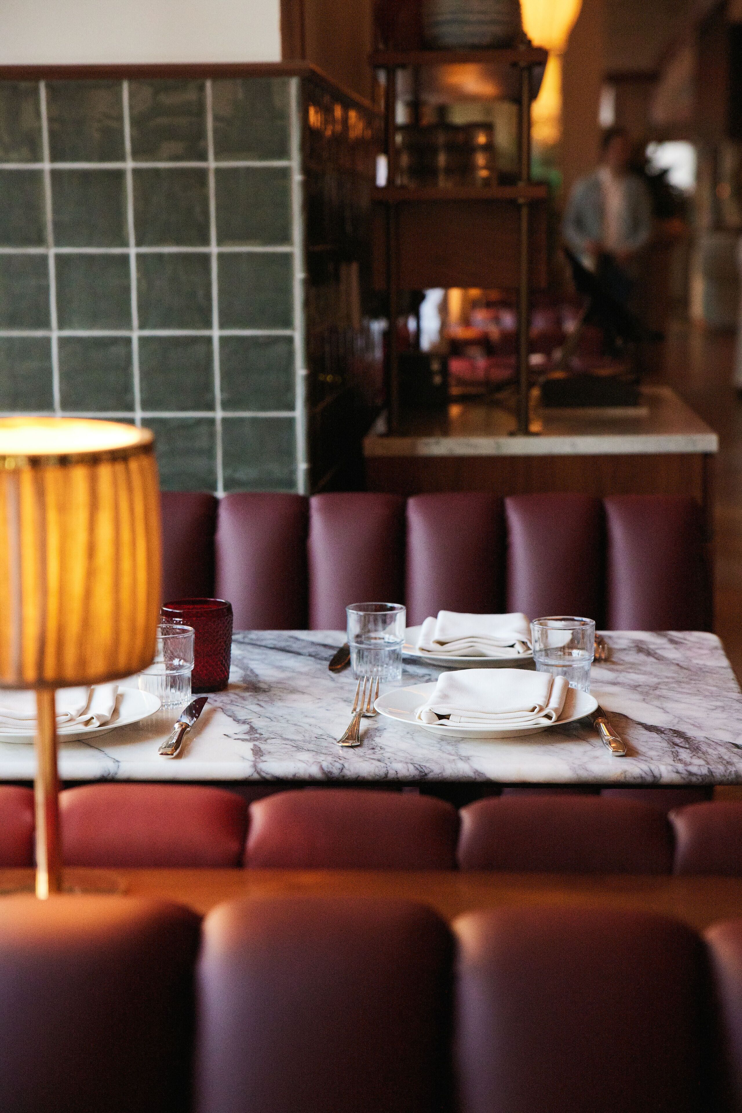 A restaurant setting with a marble table, red upholstered booths, and a tiled backsplash.