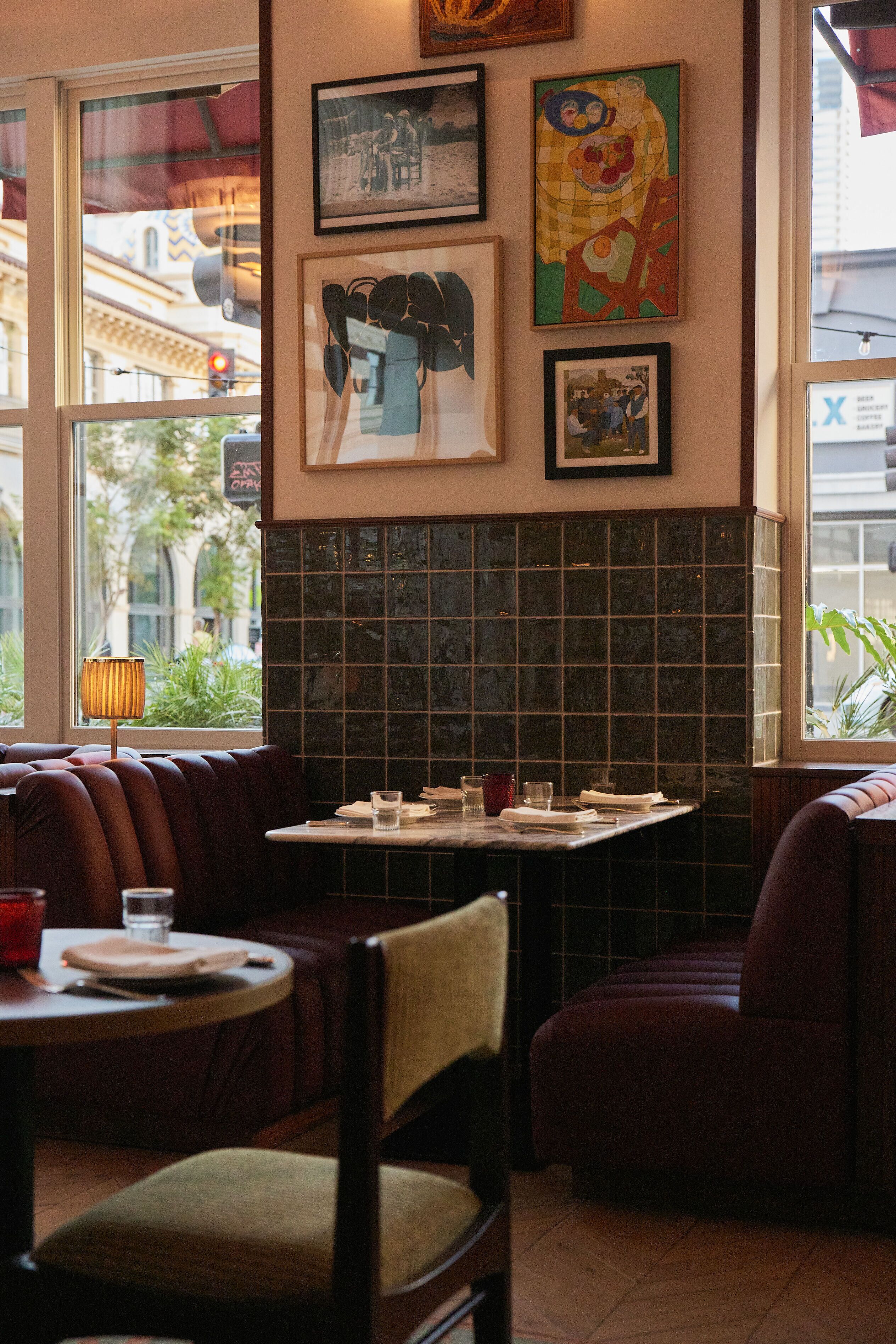 Interno di un ristorante con sedute a cabina, una parete rivestita di piastrelle e opere d'arte incorniciate alle pareti.