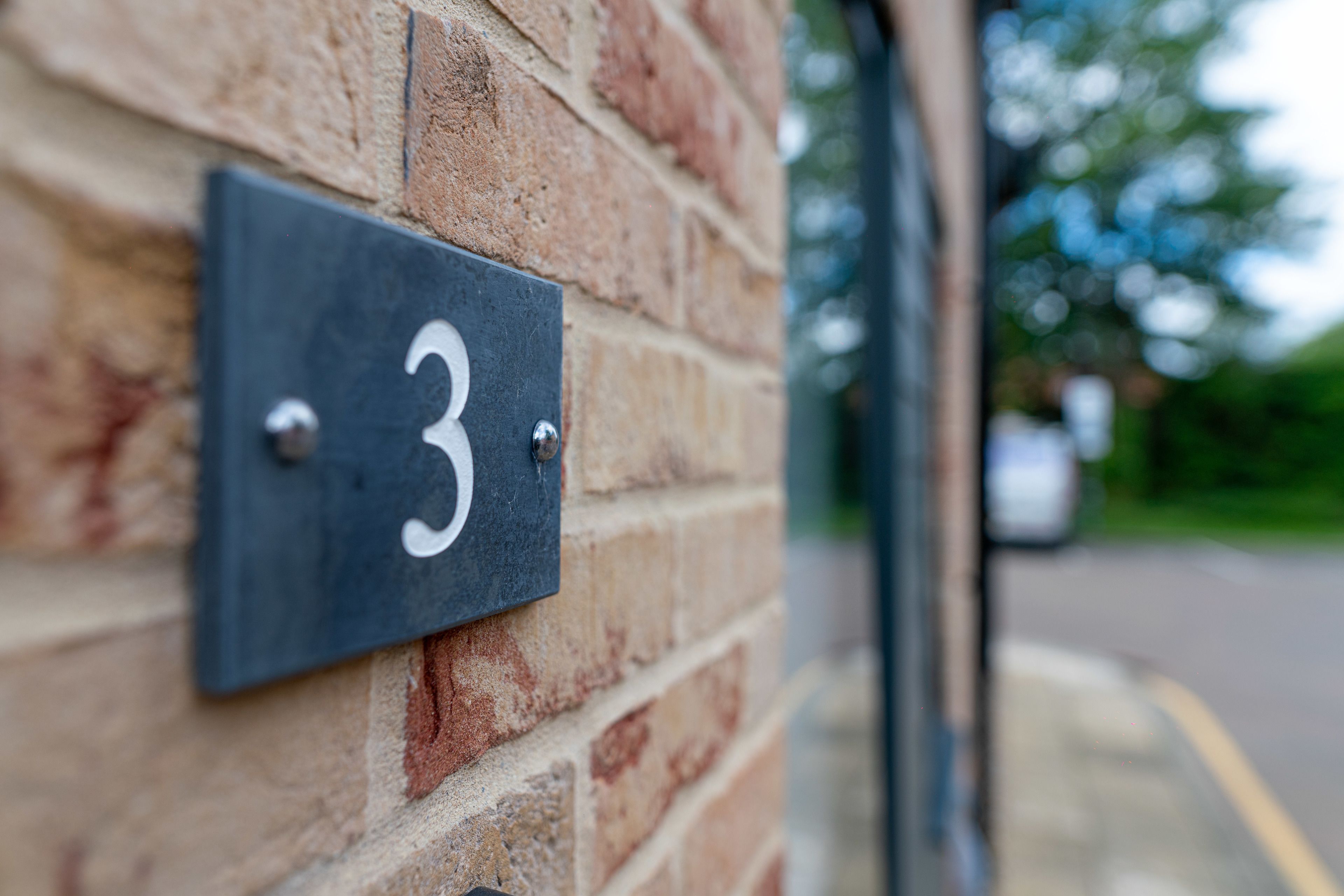 A close-up of a brick wall with a black metal sign displaying the number 3.