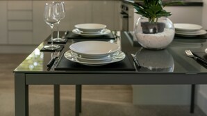 Eine moderne Küche mit Esstisch für zwei Personen, ausgestattet mit weißen Tellern, Besteck und einer Vase mit Blumen.