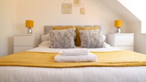 Ein ordentlich bezogenes Bett mit einem gefalteten weißen Handtuch und einer gelben Decke, zwei Nachttische mit Lampen sowie eine Wand mit aufgehängten Laternen.