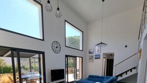 A spacious living area with a wooden dining table, blue sofa, and a staircase leading to an upper level. - Architect-designed villa, secure private pool, near center and beach  (Calvi)