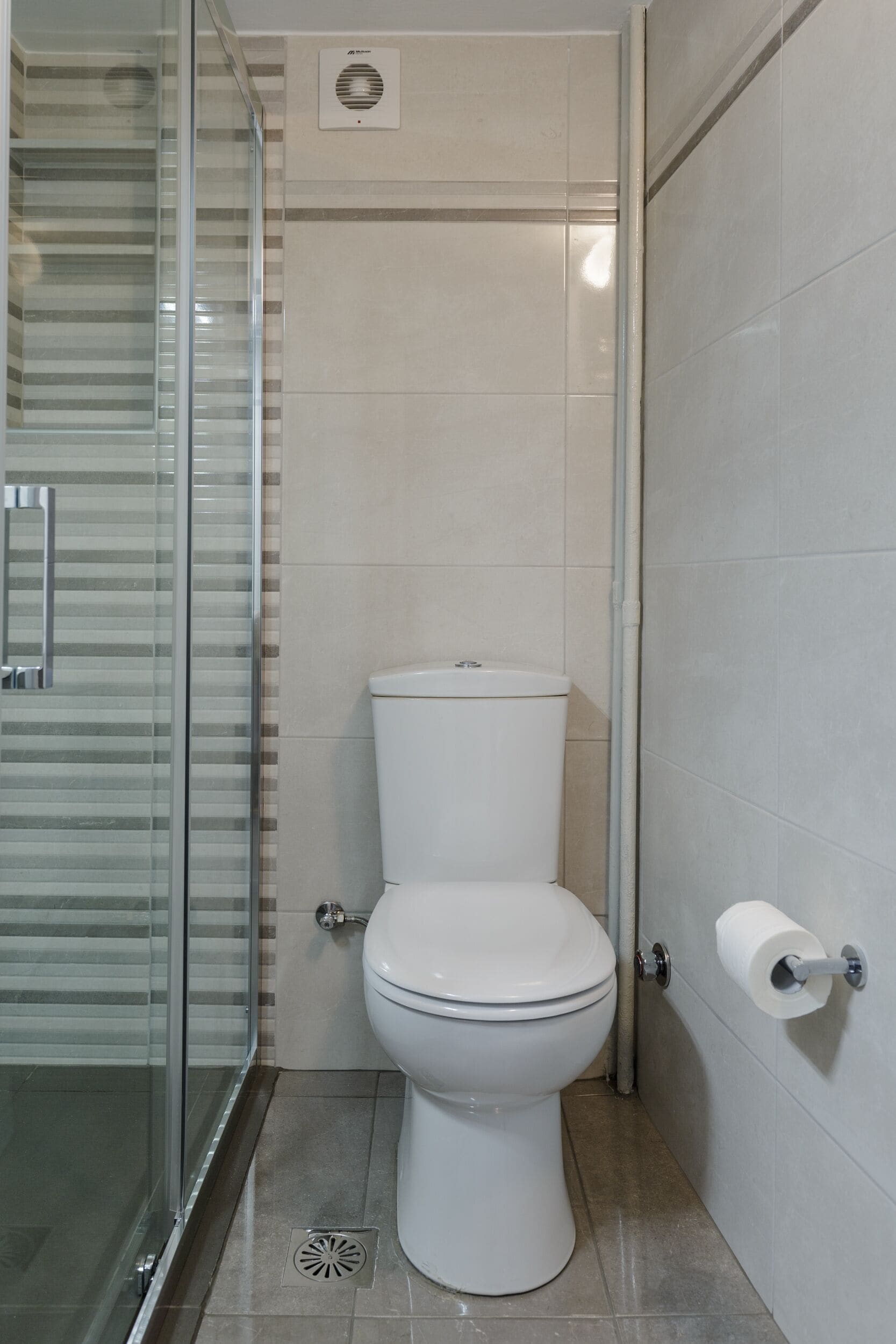 A bathroom with a glass shower enclosure, a toilet, and a wall-mounted toilet paper holder.