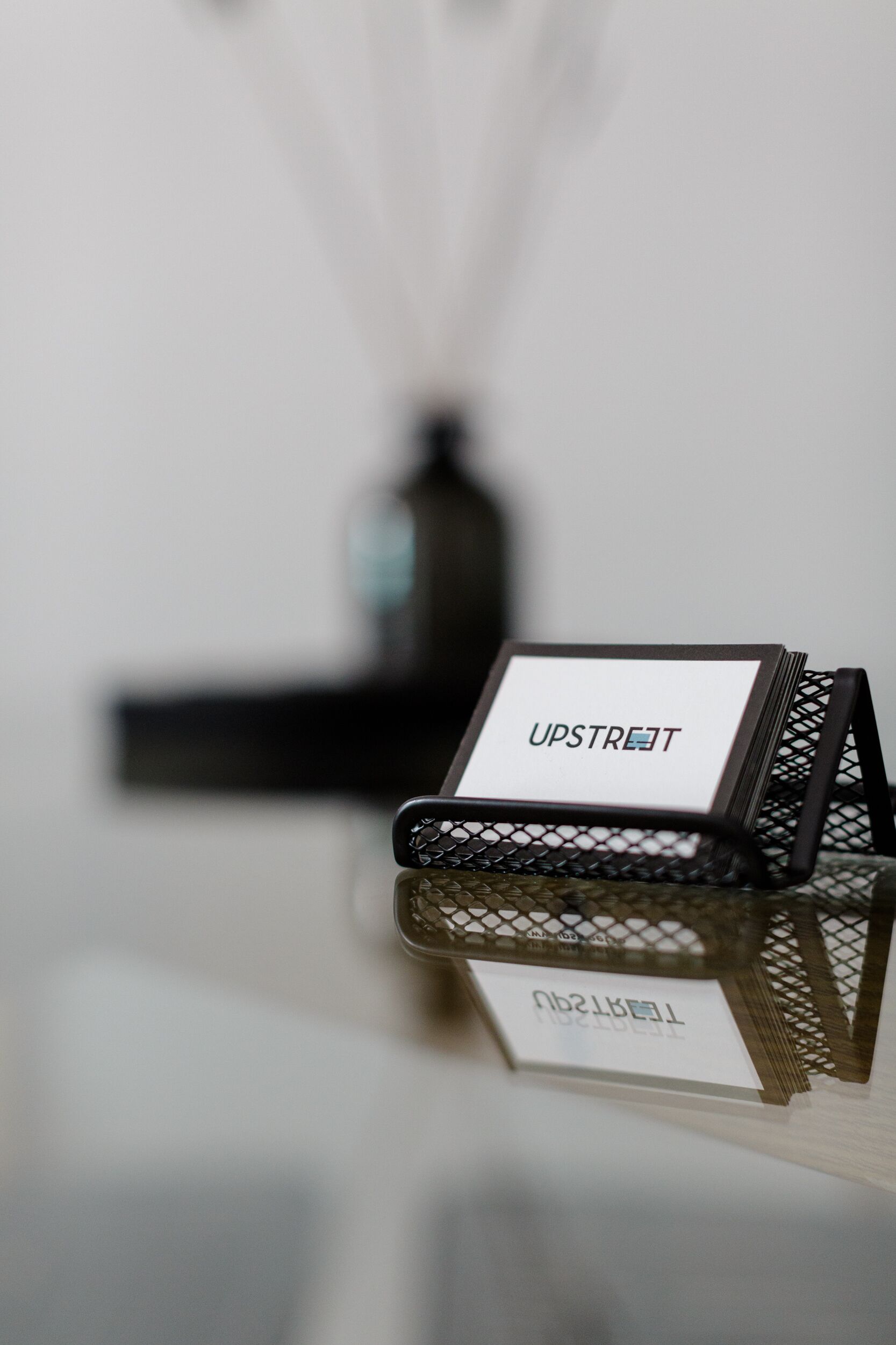 Un présentoir en métal noir avec une carte blanche portant l’inscription « UPSTREET » placée sur une surface réfléchissante.