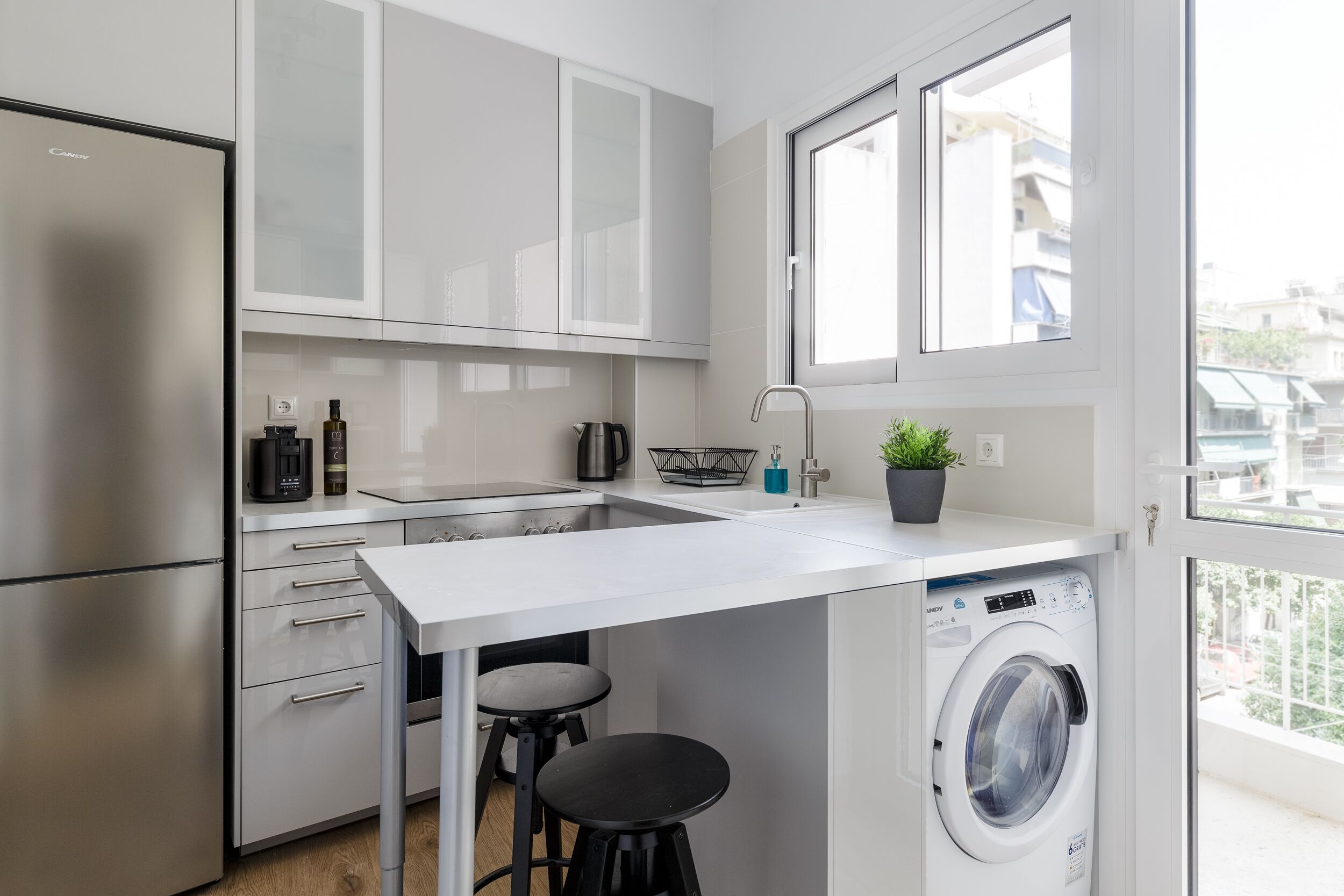Une cuisine compacte équipée d’un lave-linge intégré, d’un évier et d’une fenêtre laissant entrer la lumière naturelle.