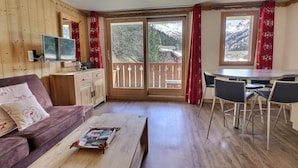 A cozy room with a wooden interior, a sofa, a coffee table, a TV, a balcony with a wooden railing, and a dining area with chairs. - 150m from ski slopes, floor -2, view mountain, balcony, 37m², Méribel-Mottaret (Méribel - Les Allues)