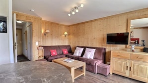 A cozy living room with a brown leather sofa, a wooden coffee table, and a TV mounted on the wall. - 150m from ski slopes, floor -2, view mountain, balcony, 37m², Méribel-Mottaret (Méribel - Les Allues)