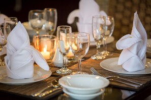 Een gedekte tafel met witte servetten, heldere wijnglazen en kaarsen, wat wijst op een formele dineropstelling.