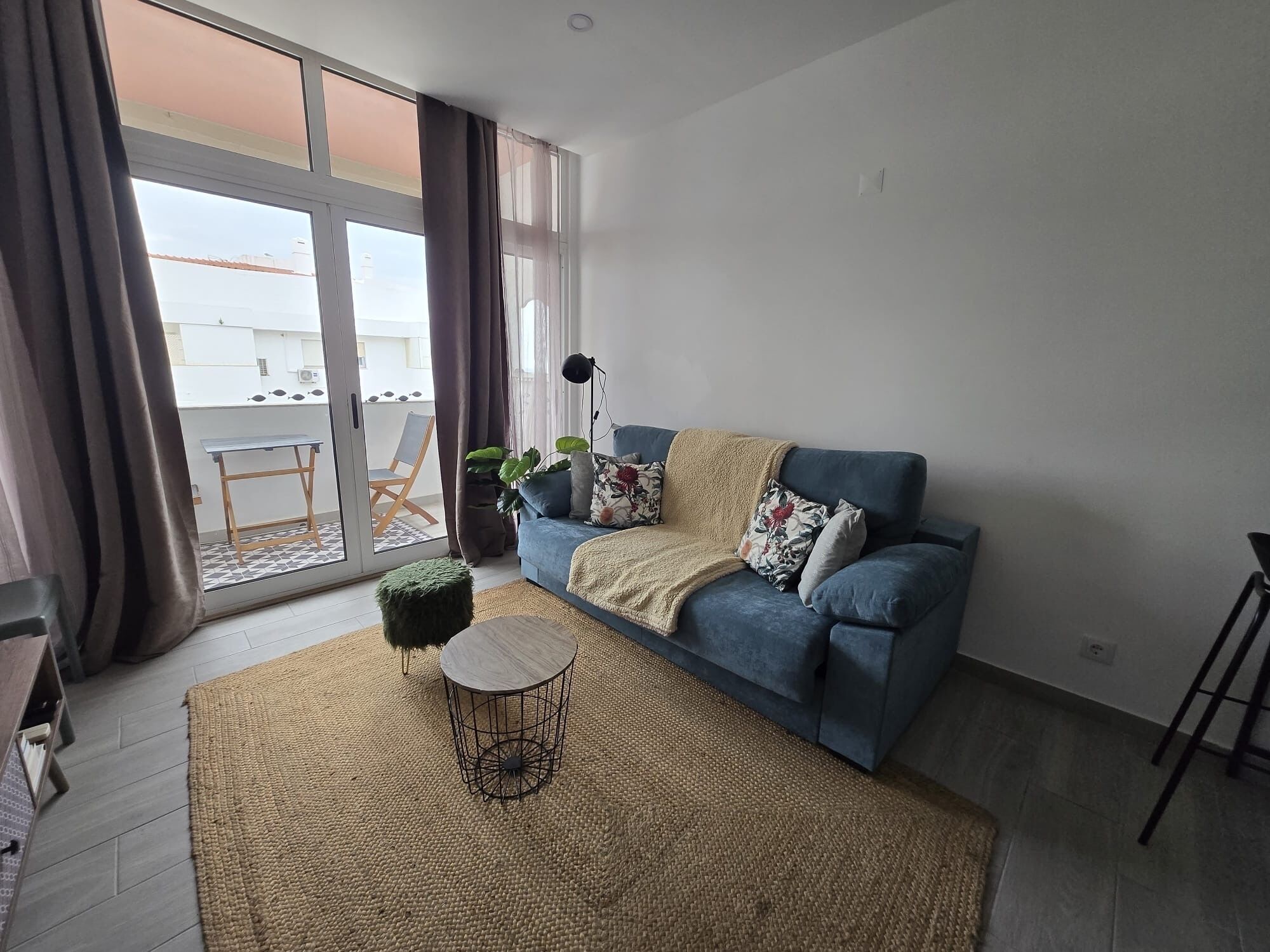 Un salon comprenant un canapé, une table basse, un balcon avec une table et des chaises, ainsi qu’une grande fenêtre.