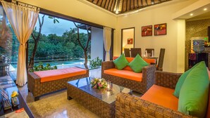 A cozy lounge area with wicker furniture, a glass coffee table, and a view of a lush garden. - 2 Bedroom villa near Pandawa Beach (Uluwatu)