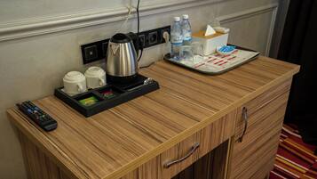 A wooden desk with a remote control, a kettle, and a tray with water bottles and a tissue box.