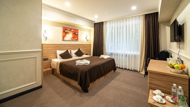 A hotel room with a large bed, a desk with a fruit bowl, and a television on the wall. - Mildom City Hotel (Almaty)