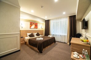 A hotel room with a large bed, a desk with a fruit bowl, and a television on the wall. - Mildom City Hotel (Almaty)