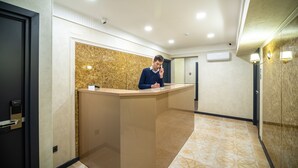 A reception desk in a hotel lobby with a marble wall, a glass partition, and a patterned floor. - Mildom City Hotel (Almaty)